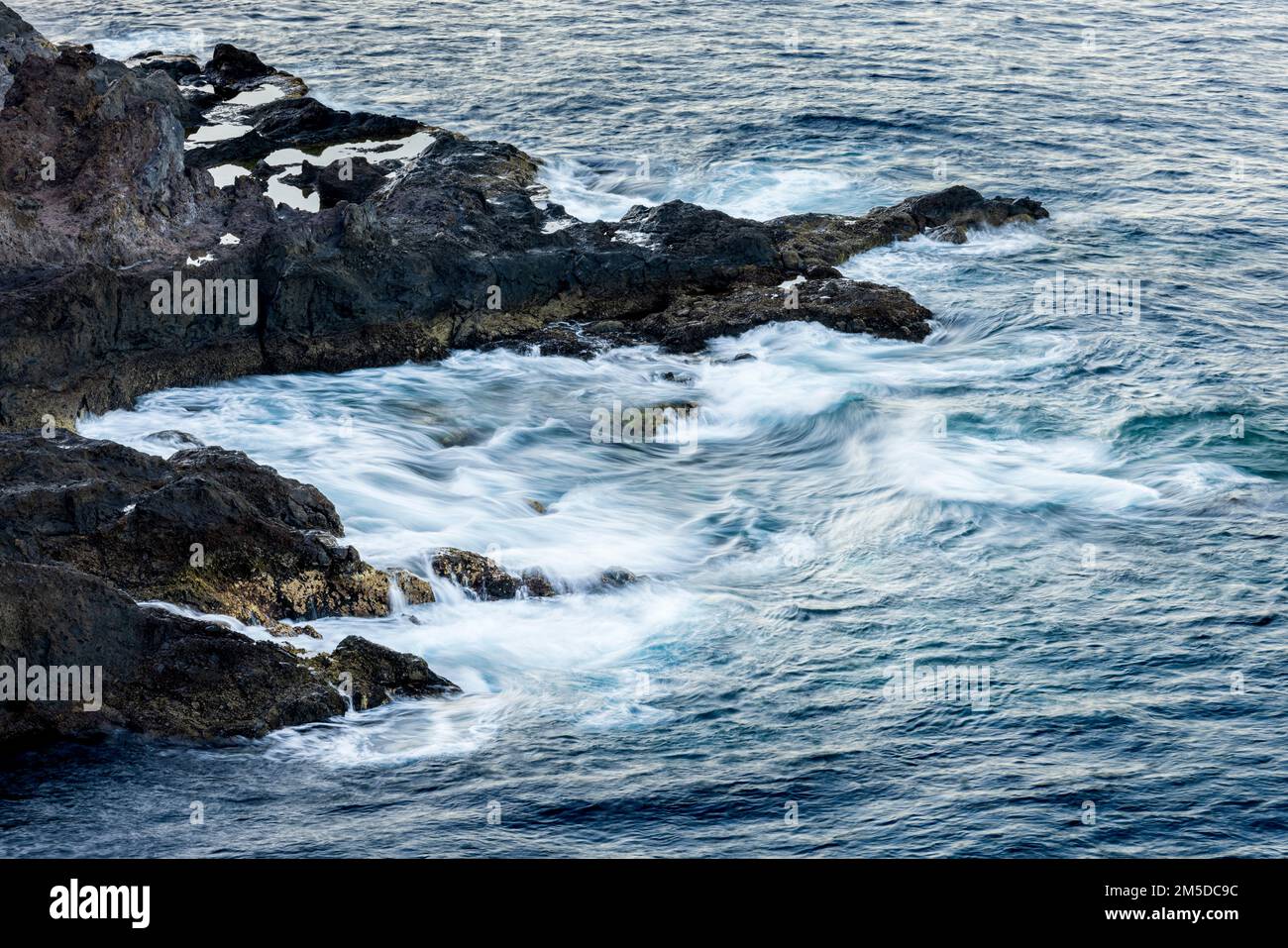Langzeitaufnahme des Atlantiks, der sich um schroffe Vulkanfelsen an der Westküste von Teneriffa, Kanarische Inseln, Spanien, dreht Stockfoto
