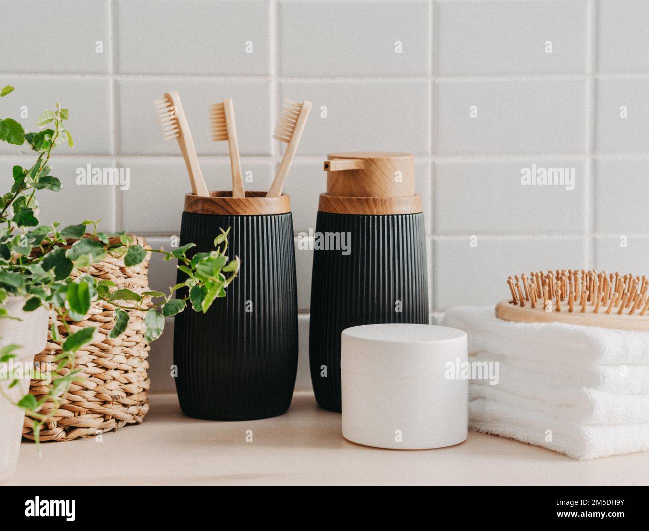 Vorderansicht des Badhintergrunds mit Strohbox, Behälter mit Zahnbürsten, Spender, Kosmetik, Holzkamm und weißen Handtüchern auf weißem Hintergrund. Vorn vi Stockfoto