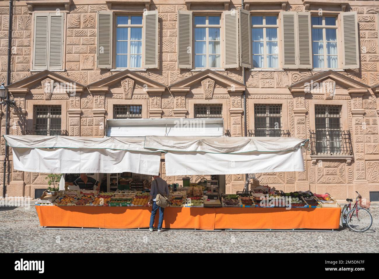 Lebensmittelmarkt, Blick im Sommer auf einen Mann, der Obst an einem Stand vor dem Palazzo Canossa auf der Piazza Matilde Canossa, Mantua, Italien kauft Stockfoto