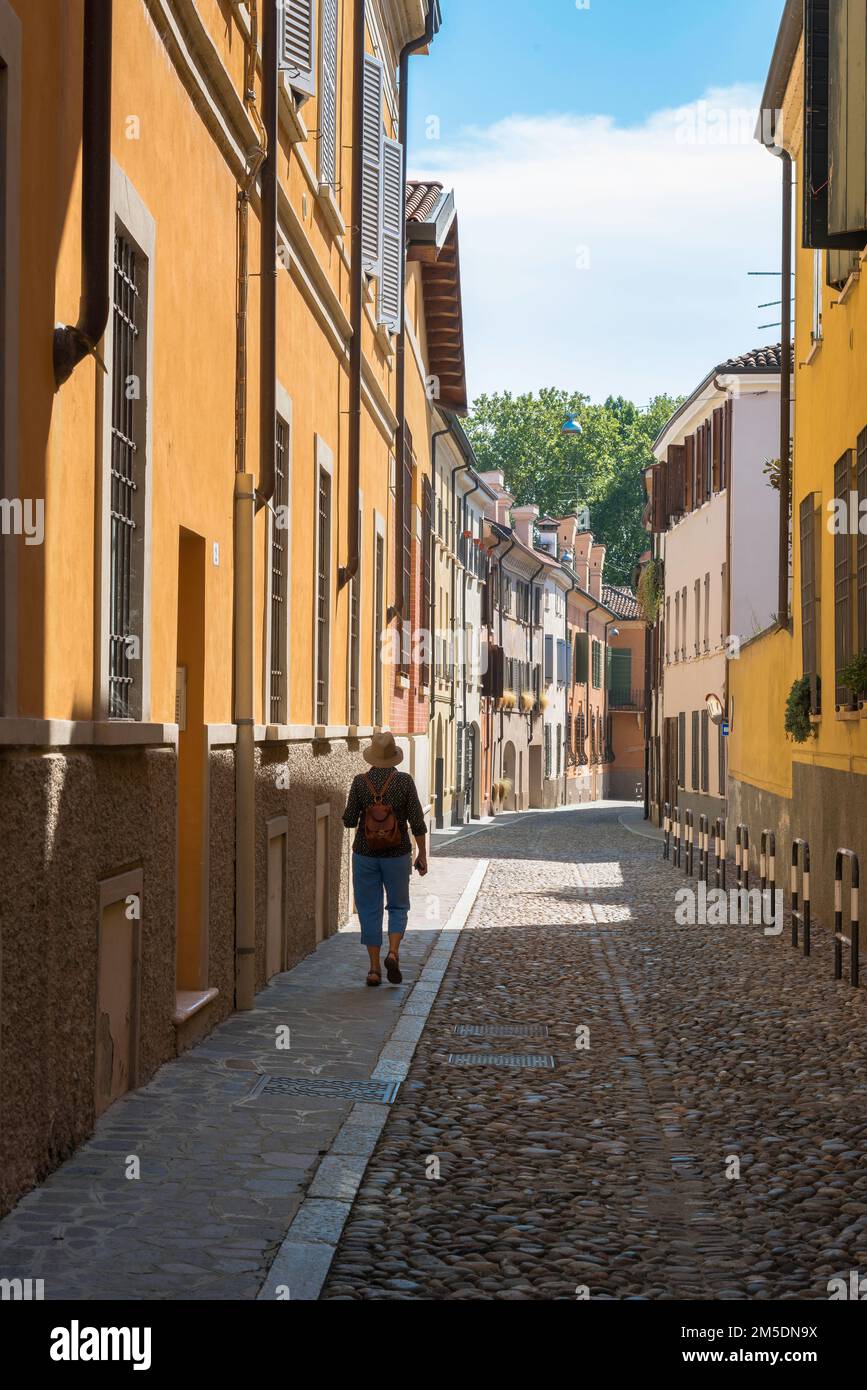 Frauenurlaub allein, Rückblick auf eine weibliche Reisende mittleren Alters, die alleine in einer Kopfsteinpflasterstraße in der malerischen Altstadt von Mantua, Italien, spaziert Stockfoto