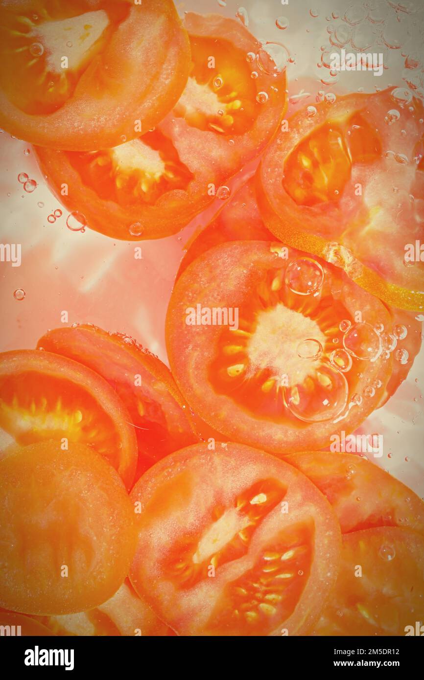 Nahaufnahme frischer Tomatenscheiben auf weißem Hintergrund. Tomatenscheiben in sprudelndem Wasser auf weißem Hintergrund, Nahaufnahme. Vertikales Bild Stockfoto