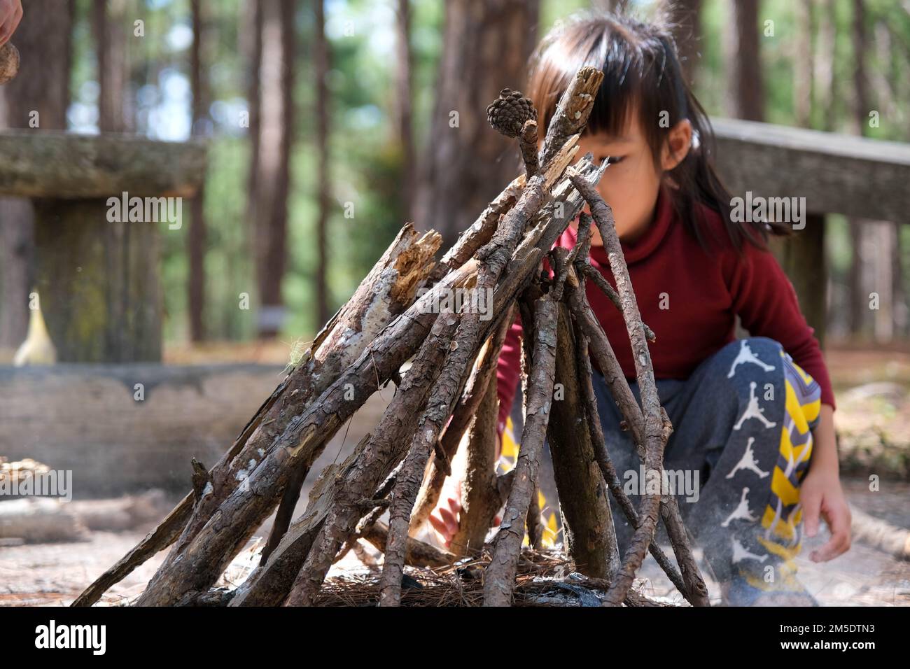 Süße kleine Schwestern machen Lagerfeuer in Naturwäldern. Kinder haben Spaß am Lagerfeuer. Camping mit Kindern im Winterkiefernwald. Glückliche Familie auf VA Stockfoto