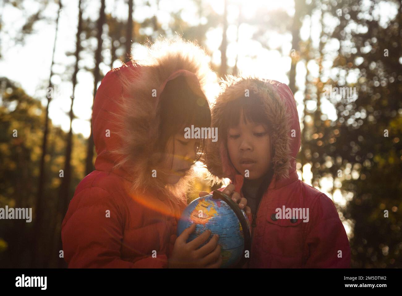 Zwei süße asiatische Mädchen lernen ein Modell der Welt im Naturhintergrund und warmes Sonnenlicht im Park. Kinder lernen durch pädagogische Aktivitäten Stockfoto