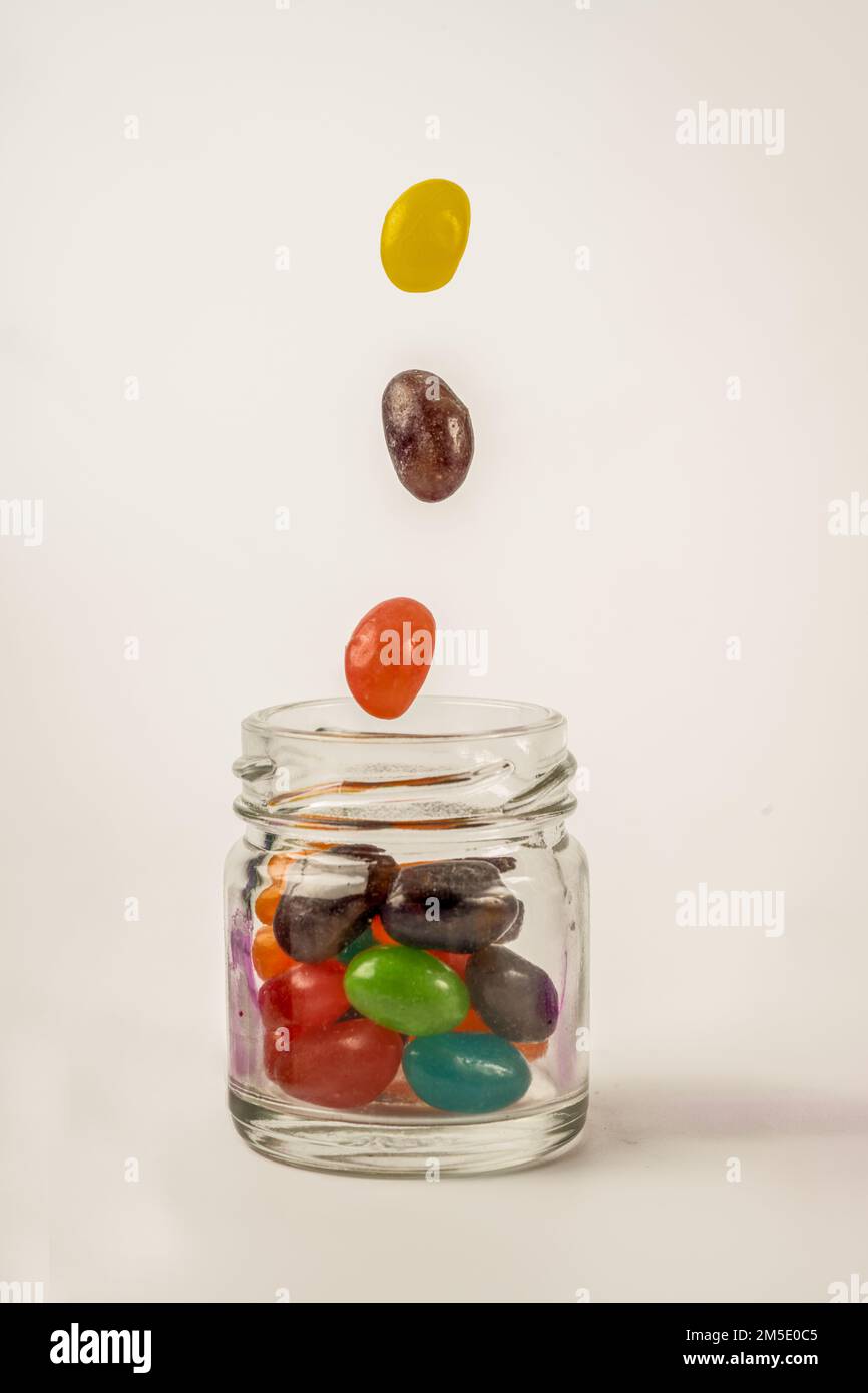 Herabfallende bunte Jelly Beans, die in einen Glasbehälter mit Schraubverschluss fallen, isoliert auf weißem Hintergrund Stockfoto