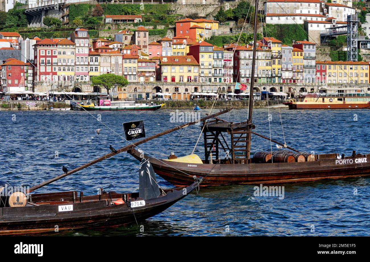 Boote auf dem Fluss Douro mit Fässern Portwein, die für Sandeman und Porto Cruz , Porto, Portugal, Europa und die Altstadt im Hintergrund werben. Stockfoto