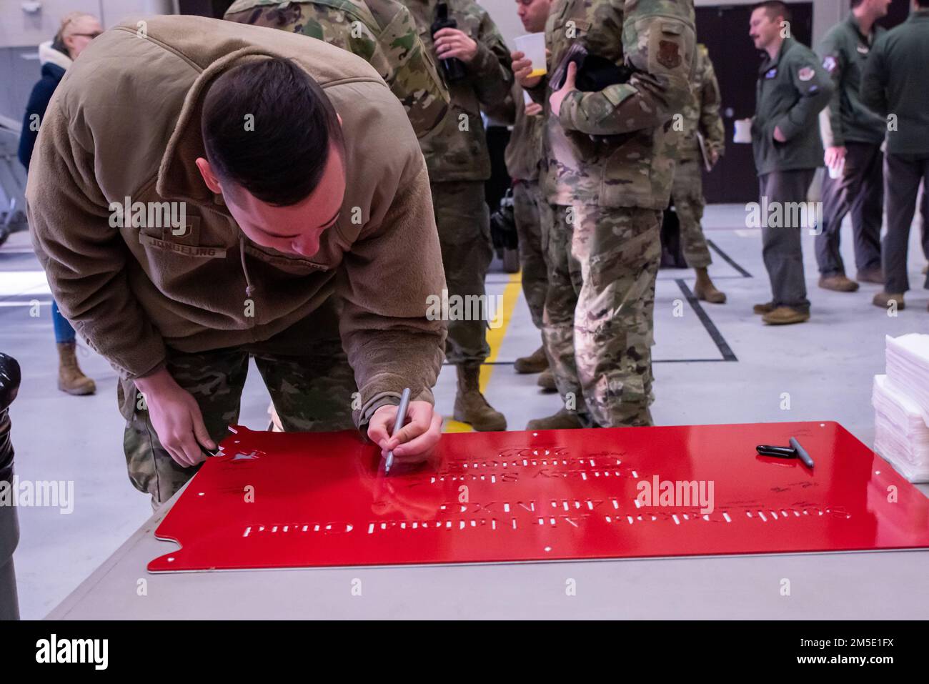 USA Air National Guard Staff Sgt. Duane Jongeling, 114. Fighter Wing Electronic Countermeasure Specialists, unterzeichnet seinen Namen auf der roten Plakette, die sein Team bei der Eröffnungsrede des Türkei Shoot auf Joe Foss Field, S.D., am 6. März 2022 erhielt. Der Zweck des Turkey Shoot war es, die Arbeitsmoral zu steigern und einen Wettbewerbsgeist innerhalb der Abteilungen Wartung und Betrieb zu schaffen. Stockfoto