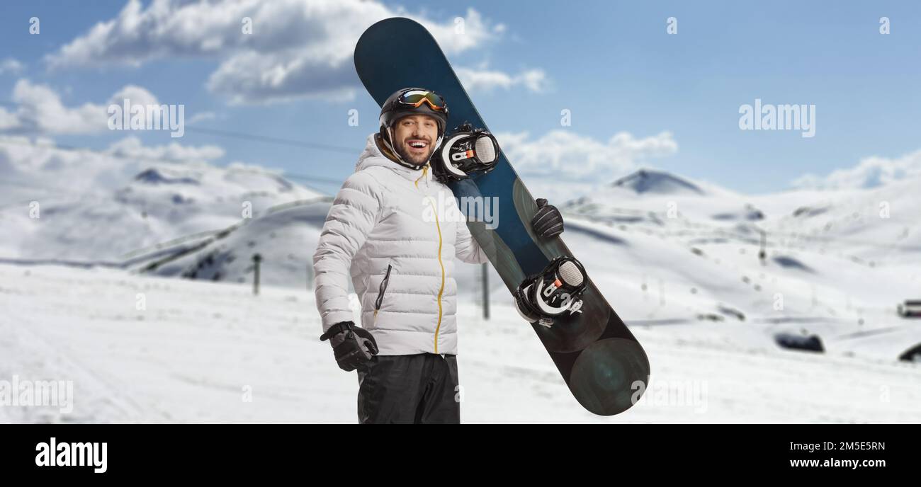 Glücklicher junger Mann mit einem Snowboard und Blick auf die Kamera auf einem Berg Stockfoto
