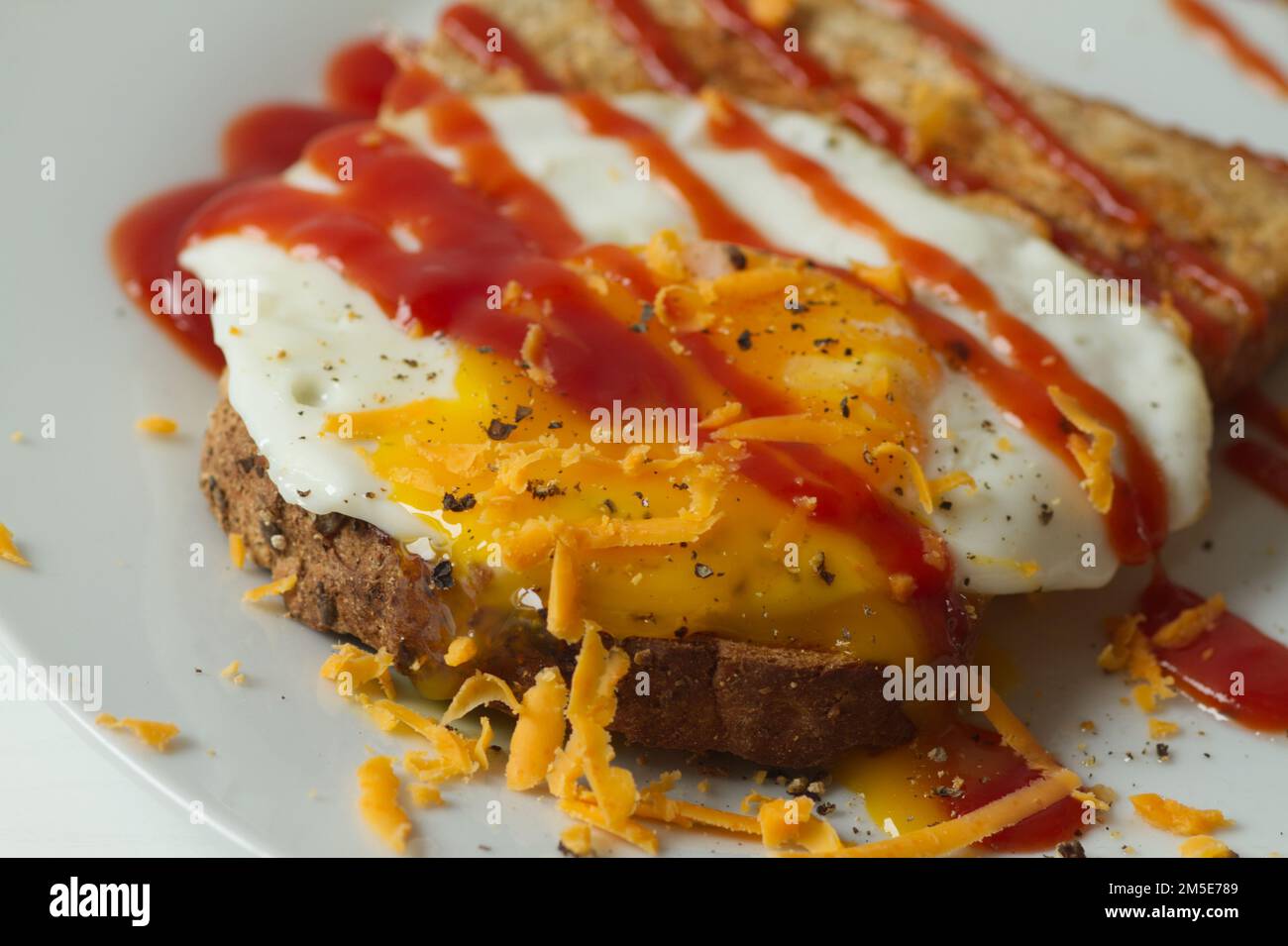 Gebratenes Ei auf einer Scheibe getoastetes Brot mit schwarzem Pfeffer, rotem Leicester-Käse und Tomatenketchup Stockfoto