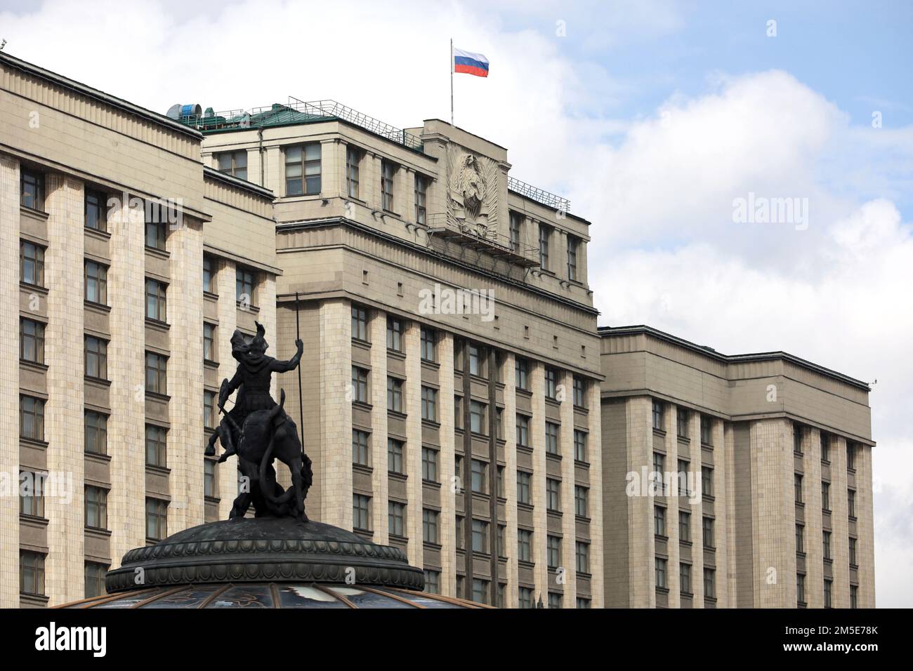 Russische Flagge auf dem Parlamentsgebäude in Moskau vor dem wolkigen blauen Himmel. State Duma und Statue of St. George der Sieger Stockfoto