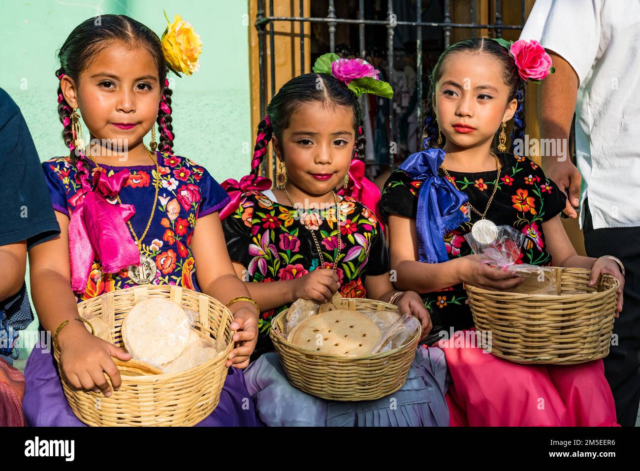 Drei kleine Mädchen in typischen Kleidern aus dem Isthmus von Tehuantepec warten auf eine Parade beim Guelaguetza Festival in Oaxaca, Mexiko. Stockfoto