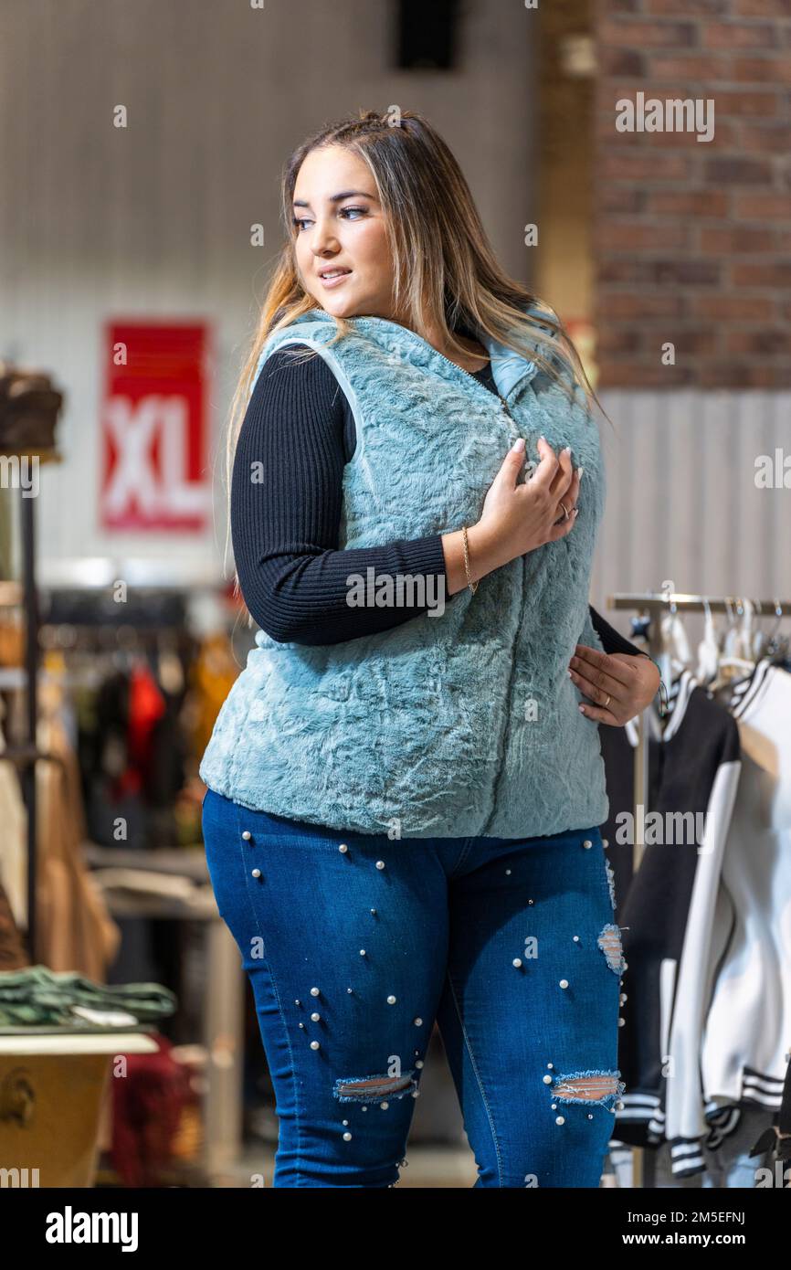 Übergewichtige Frau probiert Kleidung in einem Kleiderladen in der Übergröße-Abteilung an Stockfoto