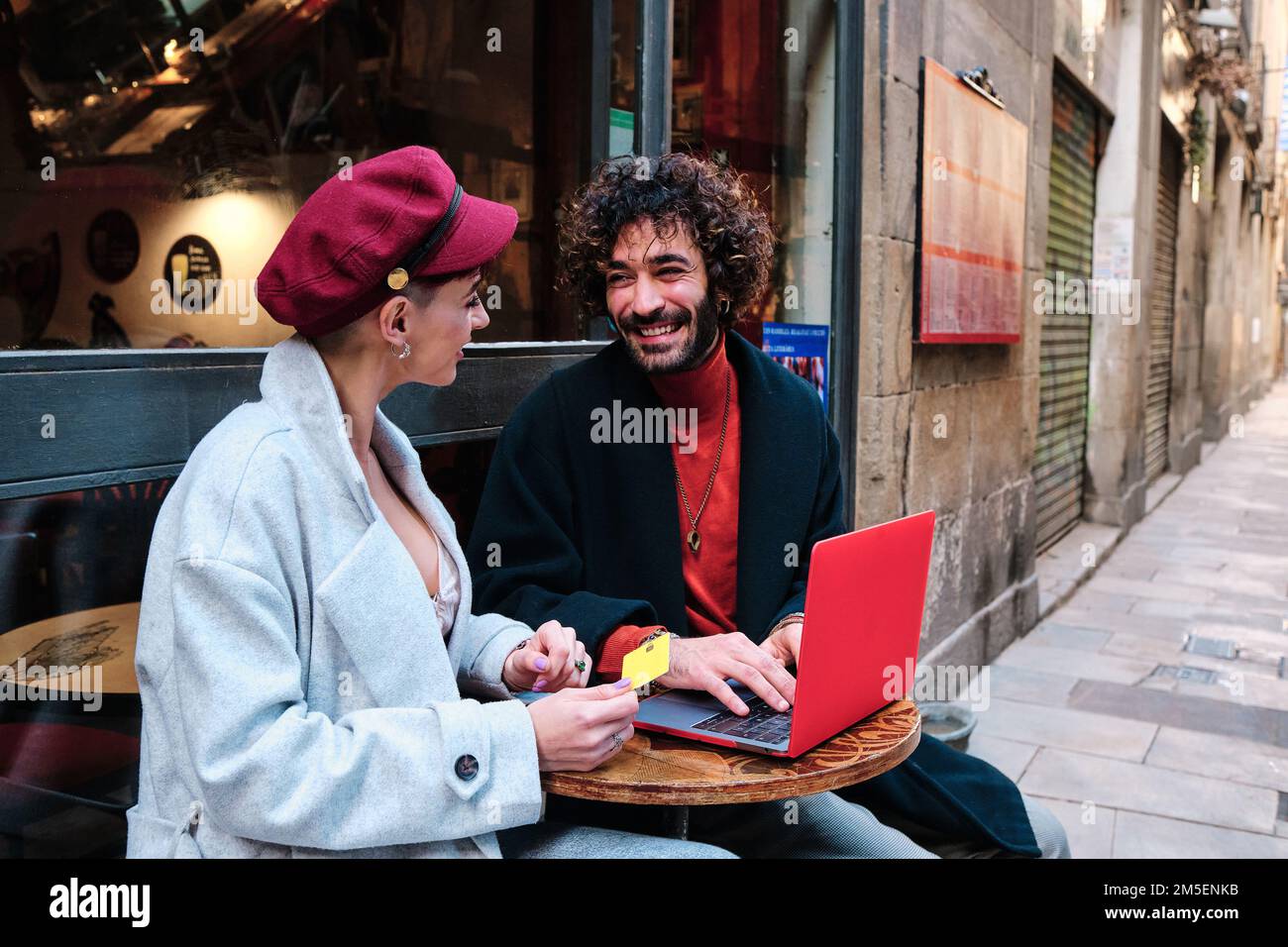Ein Paar, das online einkauft, sitzt auf der Außenterrasse der Cafeteria Stockfoto
