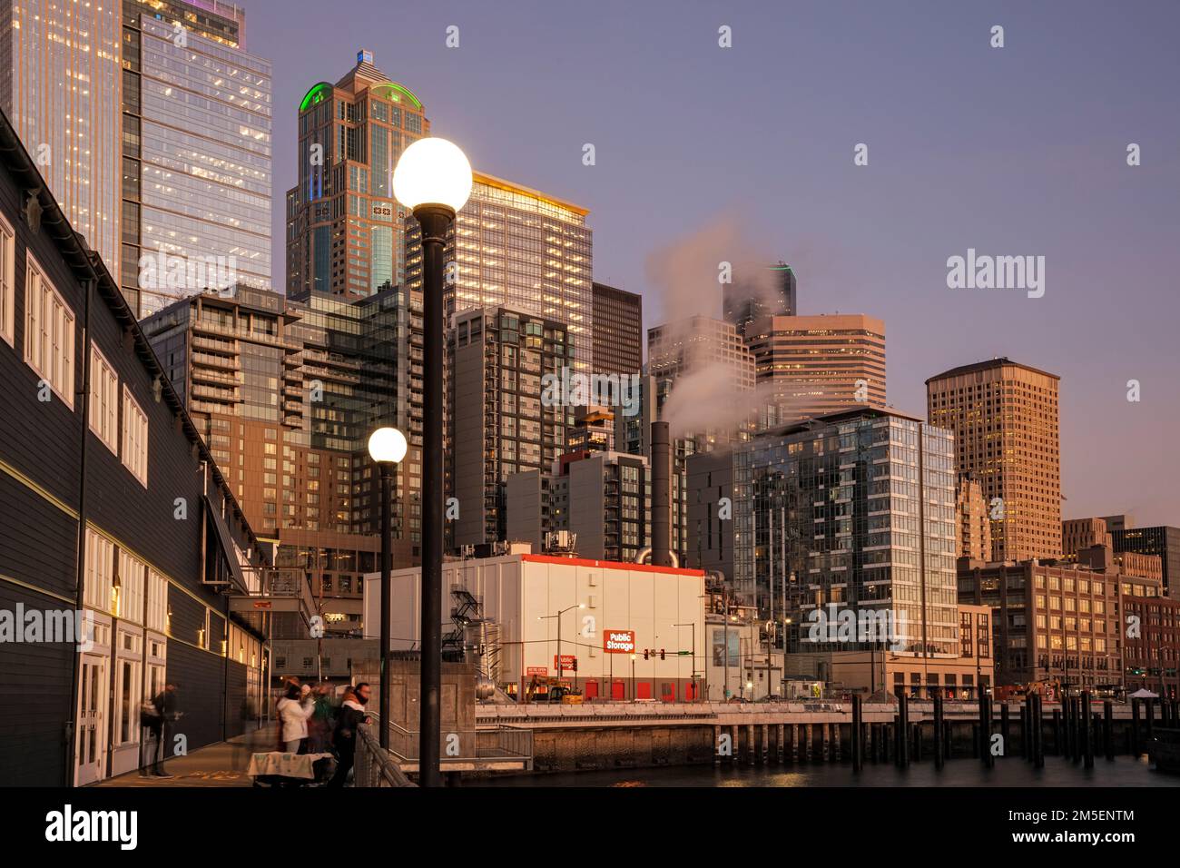 WA22873-00...WASHINGTON - Fußweg entlang der Seite des Seattle Aquarium an der Elliott Bay mit den Seattle Highhrises hinter dem Sonnenuntergang. Stockfoto