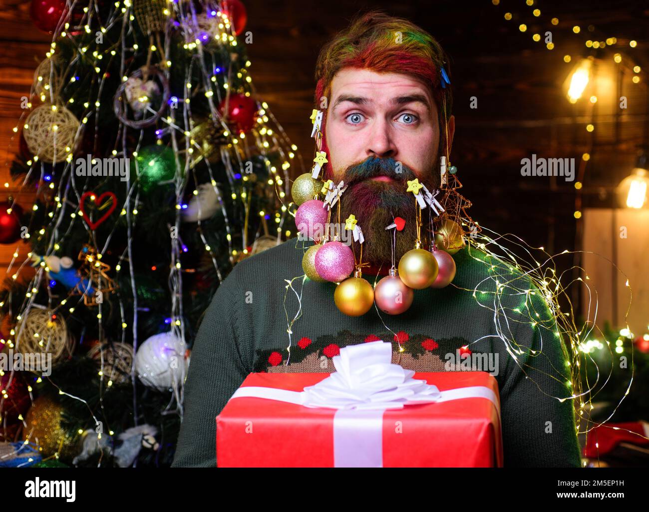 Weihnachtsbartdekorationen. Überraschter bärtiger Mann mit Geschenkbox. Neujahrsfeiertage. Stockfoto