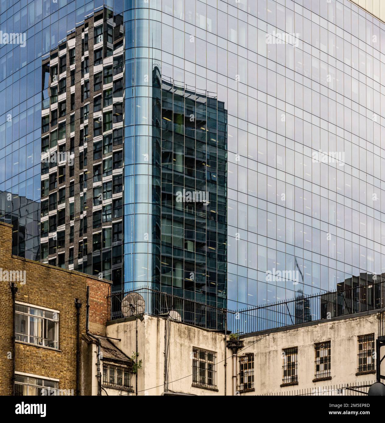 Reflexionen eines modernen Gebäudes mit alten Blöcken im Vordergrund Stockfoto