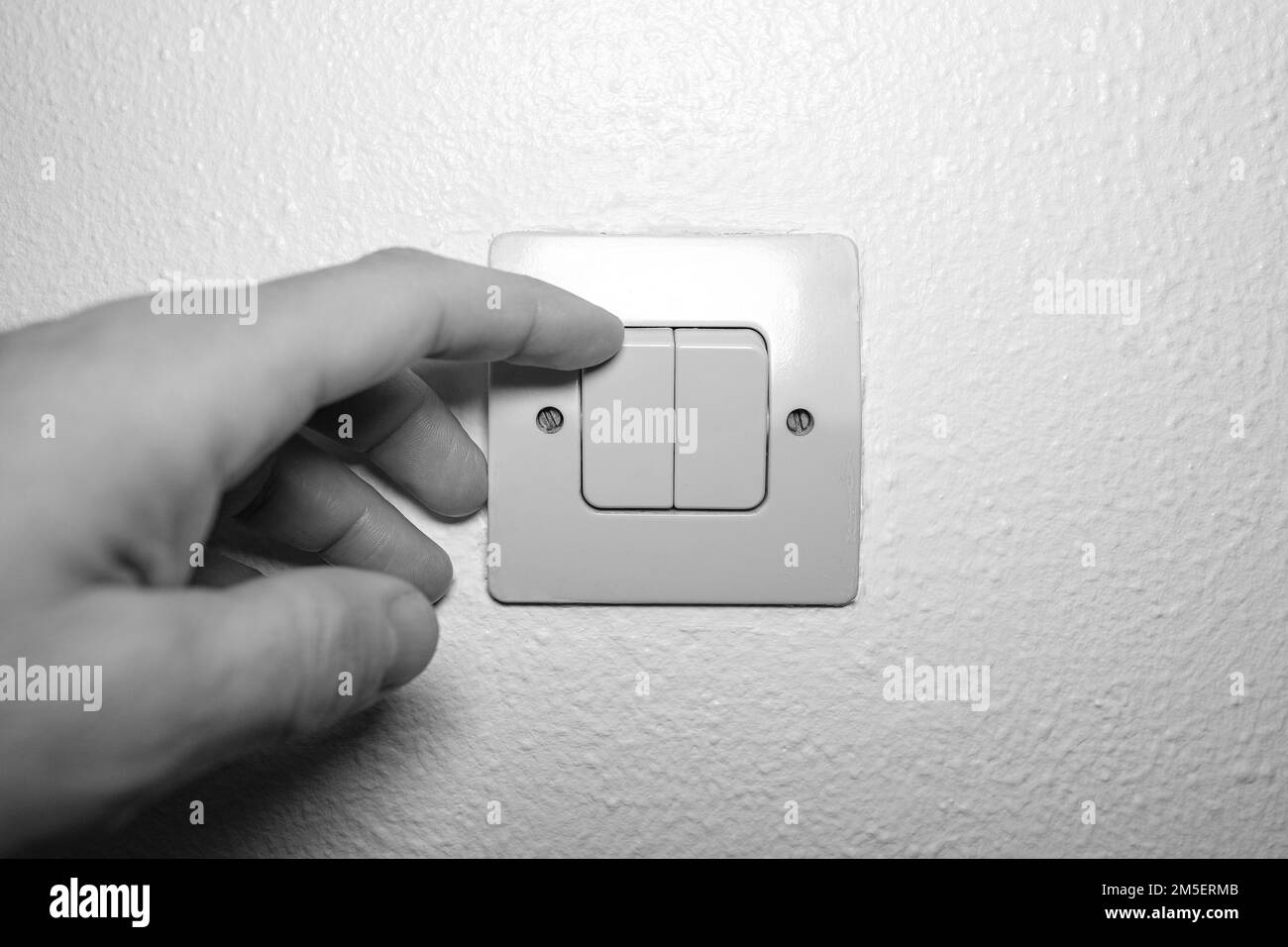 Steigende Stromkosten in der Krise, Mann schaltet zu Hause das Licht ein, Nahaufnahme von Hand in Schwarz-Weiß Stockfoto