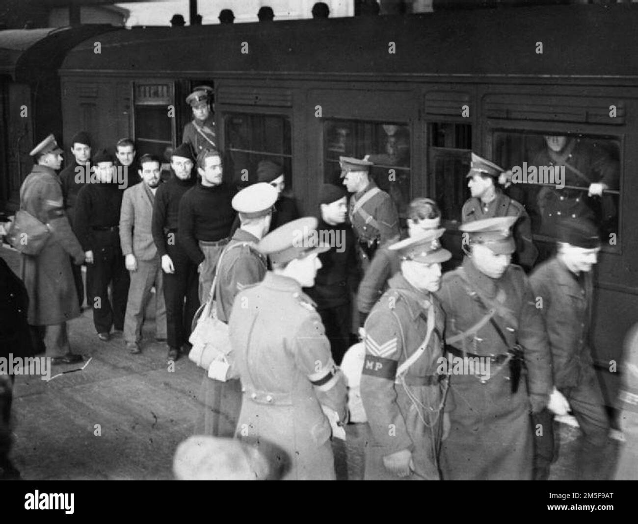 Deutsche Kriegsgefangene werden von der britischen Militärpolizei aus ihrem Zugwagen und entlang des Bahnsteigs an einem Londoner Bahnhof (möglicherweise Euston) begleitet. Diese Gefangenen sind U-Boot-Crew und werden von einem Lager in ein anderes verlegt. Stockfoto