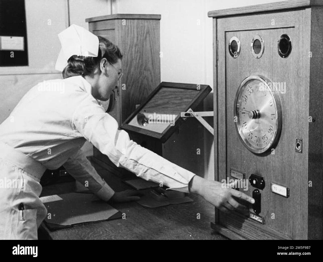 Krankenschwester schaltet das Radiumbehandlungsgerät in einem Londoner Krankenhaus 1940 ein. Wenn der Patient bereit ist und alle anderen den Bestrahlungsraum verlassen haben, drückt die Krankenschwester eine Taste, und der Luftdruck überträgt das Radium erneut vom Elektrodensafe in das Bestrahlungsgerät. Stockfoto