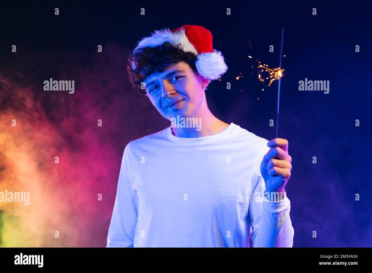 Junger Mann mit Weihnachtsmannmütze mit bengalischem Glitzerfeuer unter Neonlicht. Neujahrsfeier oder Weihnachtsfeier. Lebhafter, glücklicher Kerl. Stockfoto