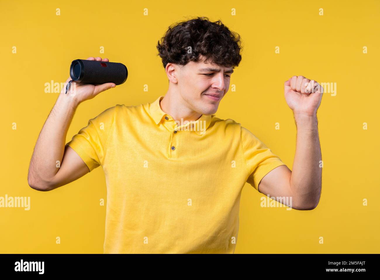 Ein Mann tanzt, genießt den gelben Studiohintergrund. Der Kerl bewegt sich zum Rhythmus der Musik. Junger Teenager, der Musik über kabellose tragbare Lautsprecher hört – Stockfoto