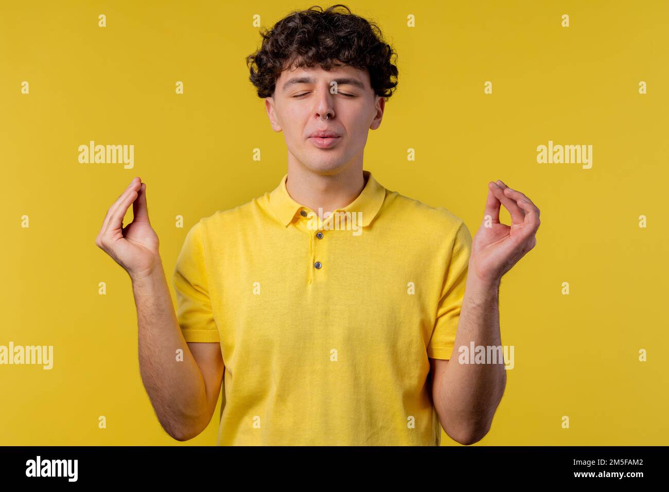 Ruhiger Mann, entspannend, meditierend, stressfrei. Ein lockiger Kerl atmet tief ein, beruhigt den gelben Studiohintergrund. Yoga, moralische Balance, Zen-Konzept Stockfoto