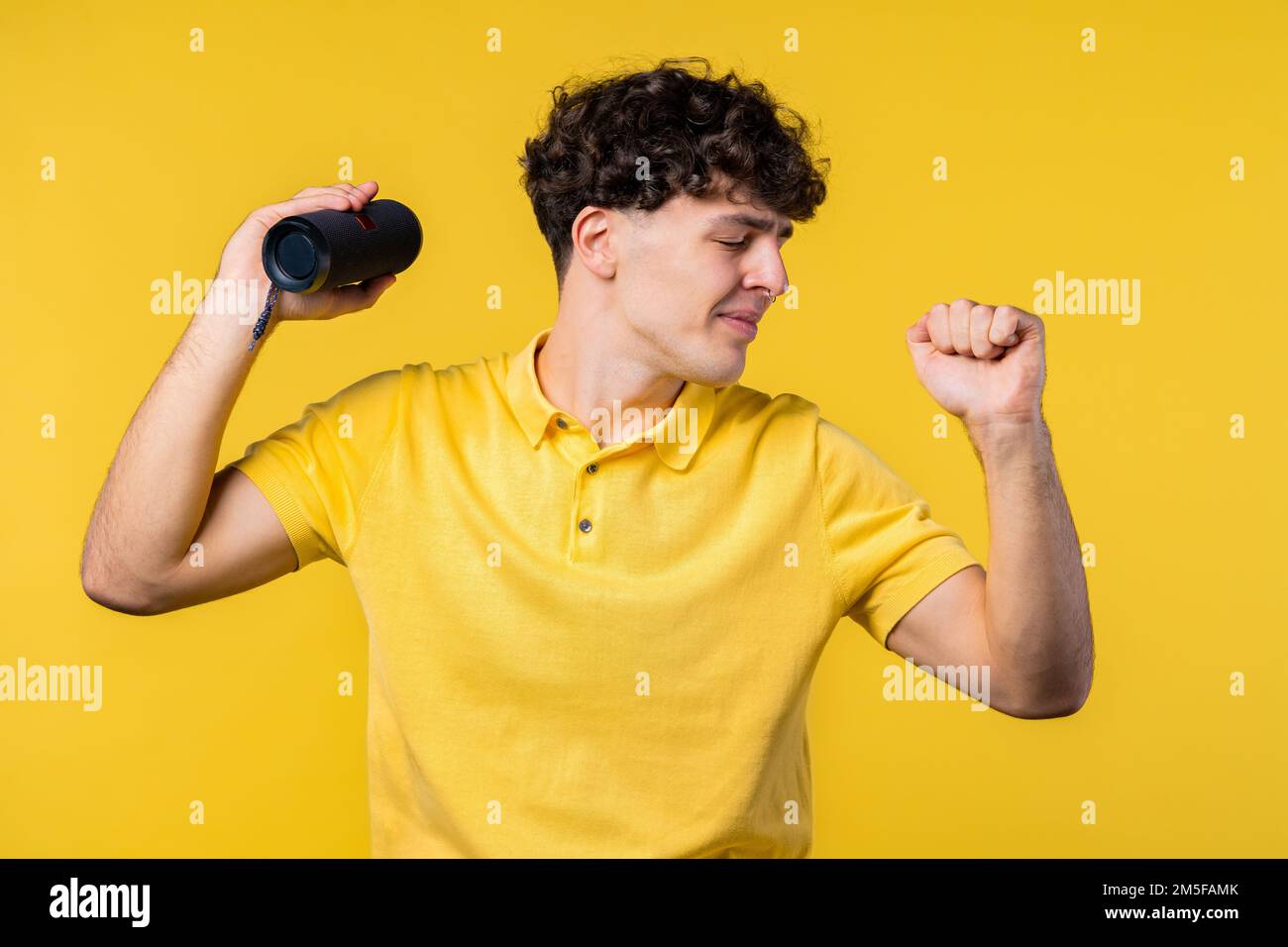 Ein Mann tanzt, genießt den gelben Studiohintergrund. Der Kerl bewegt sich zum Rhythmus der Musik. Junger Teenager, der Musik über kabellose tragbare Lautsprecher hört – Stockfoto