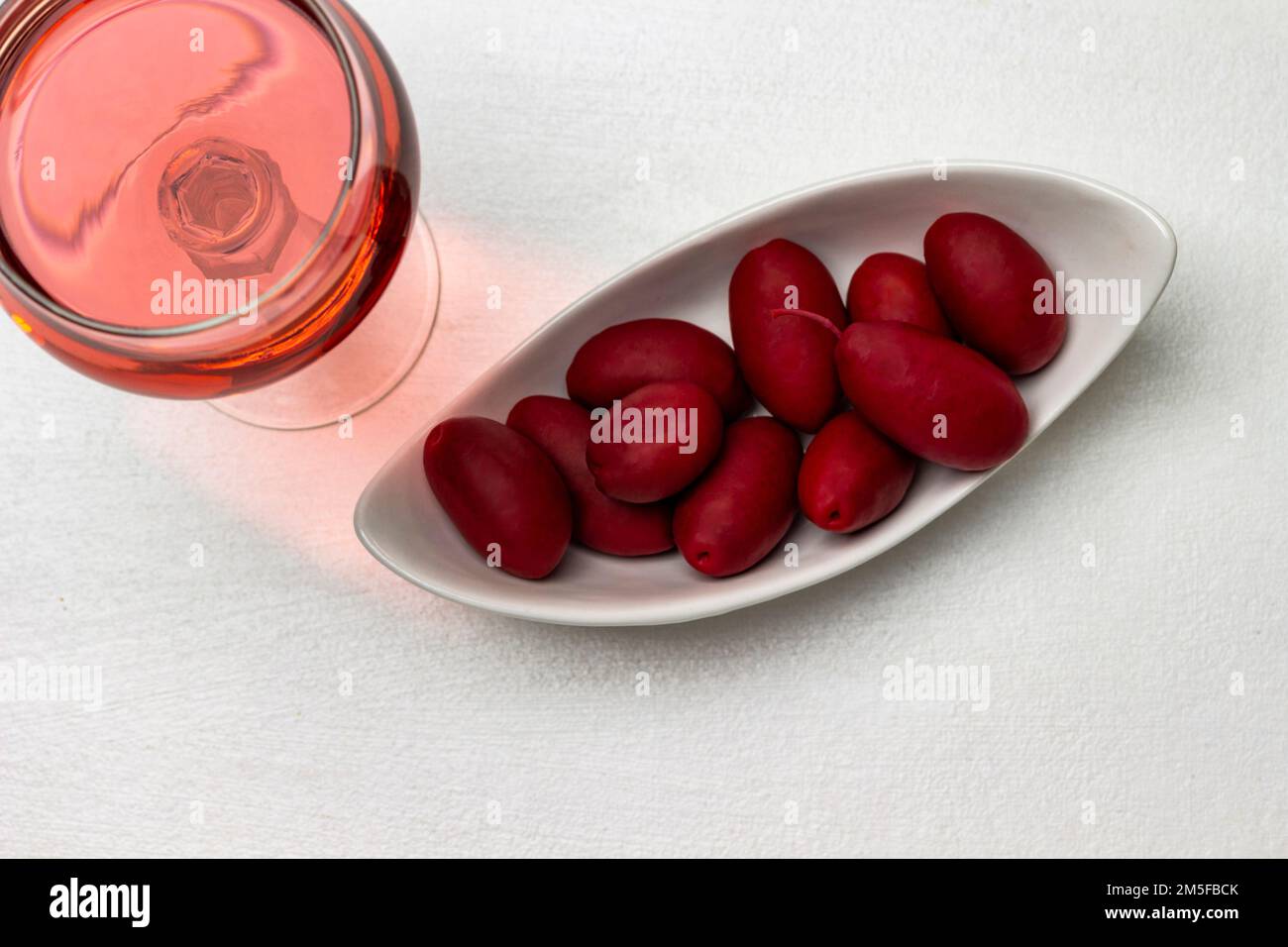 Burgunder Oliven in einer weißen Schüssel. Ein Glas mit Rosenwein. Flach verlegt. Weißer Hintergrund. Stockfoto