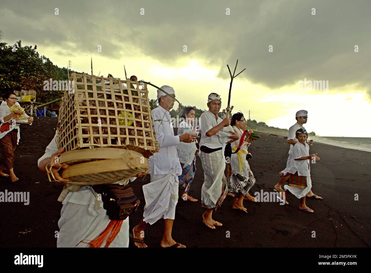Ein balinesischer Clan läuft am Sandstrand entlang, um ein Ritual zur Ehre und Reinigung der Geister ihrer verstorbenen Familienmitglieder durchzuführen, an einem Strand in der Nähe des Goa Lawah Tempels in Dawan, Klungkung, Bali, Indonesien. Stockfoto