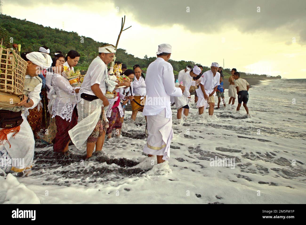 Ein balinesischer Clan, der ein Ritual durchführt, um die Geister seiner verstorbenen Familienmitglieder zu ehren und zu reinigen, an einem Strand in der Nähe des Goa Lawah Tempels in Dawan, Klungkung, Bali, Indonesien. Stockfoto