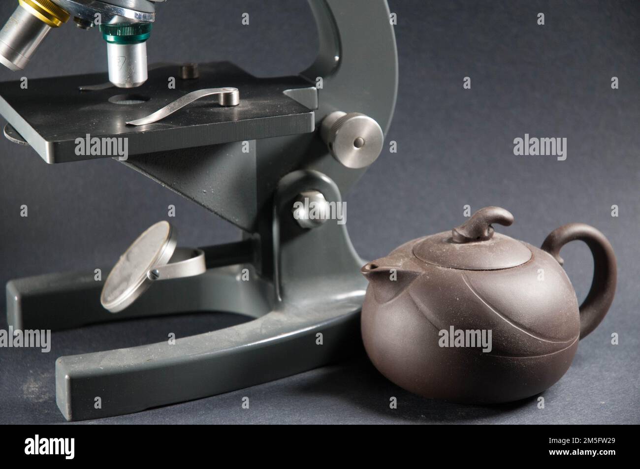 Eine Yixing-Teekanne sitzt neben einem alten Mikroskop vor grauem Hintergrund. Trennung, keine Verbindung. Stockfoto
