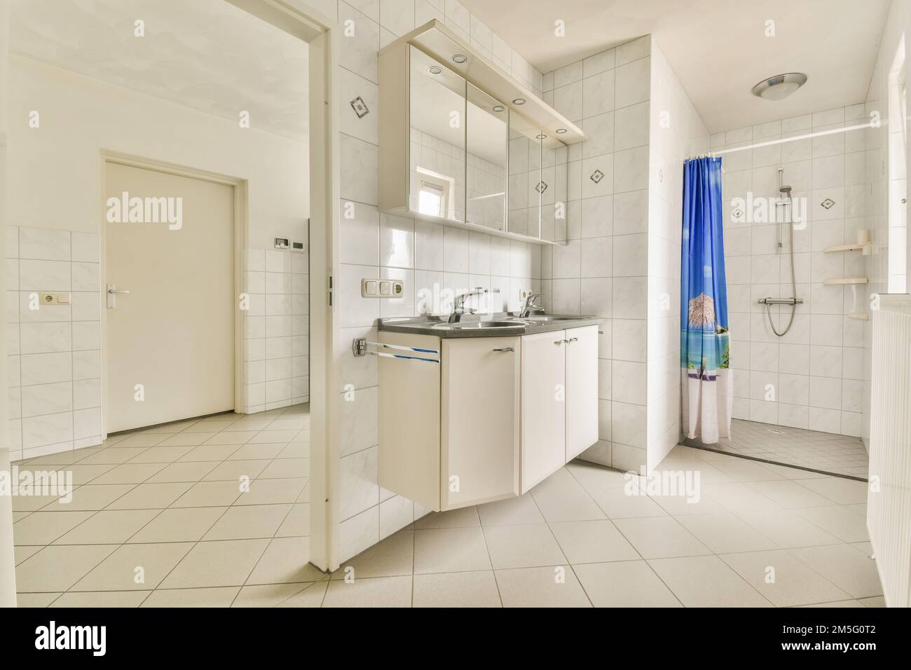 Ein Badezimmer mit weißen Fliesen und blauem Duschvorhang am Fenster vor dem Waschbecken Stockfoto