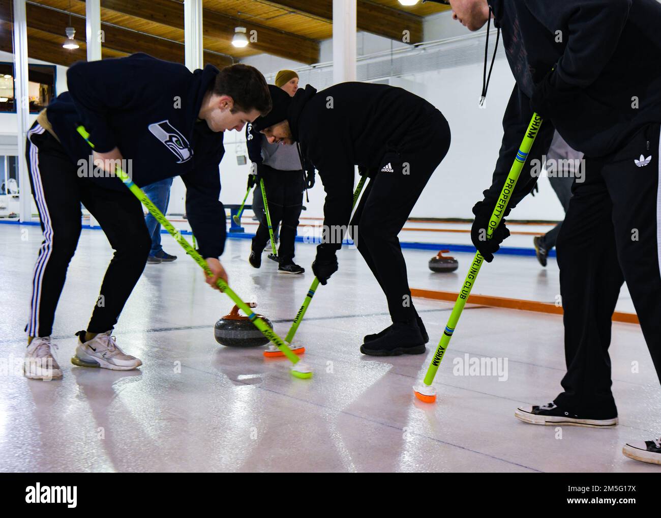 Am 15. März 2022 im Minot Curling Club in Minot, North Dakota, fegen die Flugzeuge der Minot Air Force Base das Eis, um die Reibung des Eiss und die Locken des Steins zu kontrollieren und die Mitte des Knopfs zu erreichen. Lockensteine wiegen 42 Pfund und müssen 150 Meter vom Spieler, der den Stein gleitet, bis zum Knopf des Hauses zurücklegen. Stockfoto
