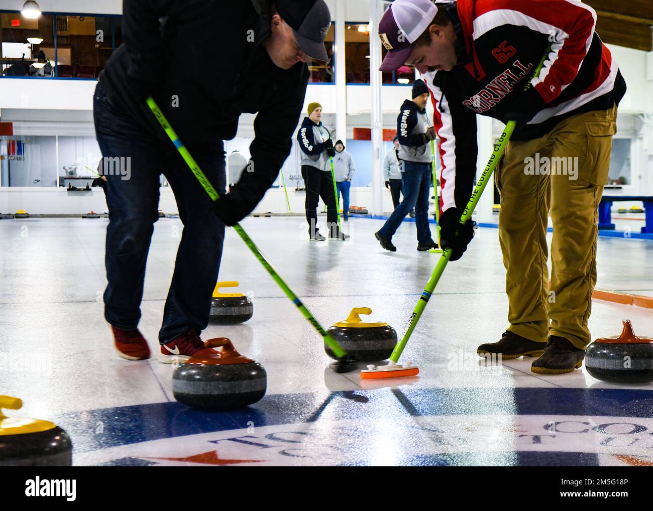 Am 15. März 2022 im Minot Curling Club in Minot, North Dakota, fegen die Flugzeuge der Minot Air Force Base das Eis, um die Reibung des Eiss und die Locken des Steins zu kontrollieren und die Mitte des Knopfs zu erreichen. Lockensteine wiegen 42 Pfund und müssen 150 Meter vom Spieler, der den Stein gleitet, bis zum Knopf des Hauses zurücklegen. Stockfoto
