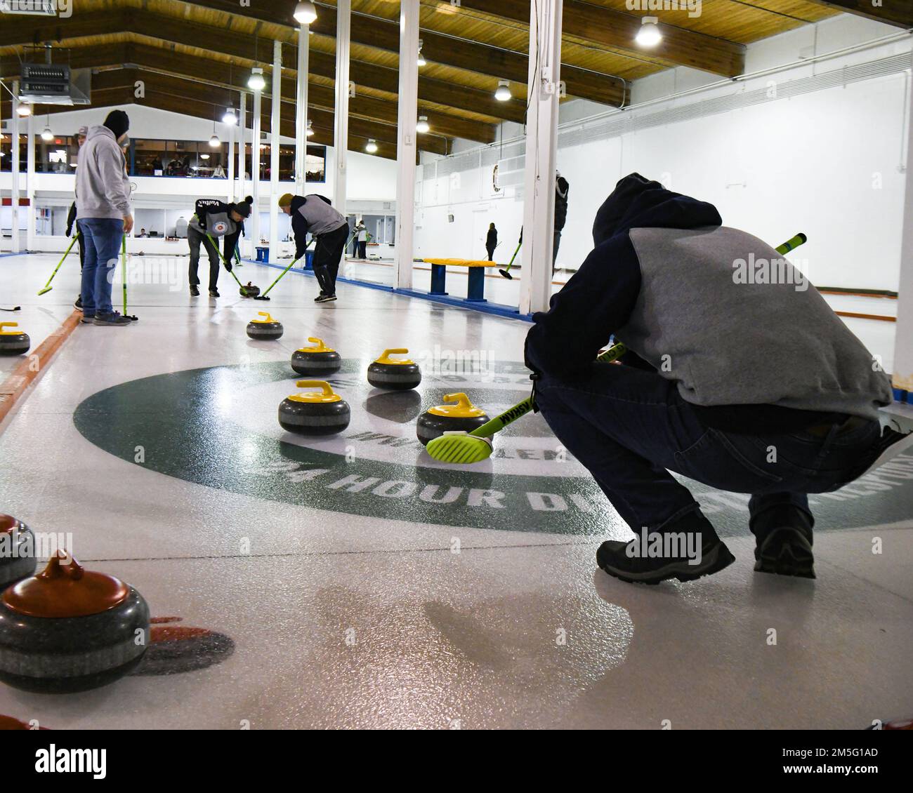 Am 15. März 2022 im Minot Curling Club in Minot, North Dakota, fegen die Flugzeuge der Minot Air Force Base das Eis, um die Reibung des Eiss und die Locken des Steins zu kontrollieren und die Mitte des Knopfs zu erreichen. Lockensteine wiegen 42 Pfund und müssen 150 Meter vom Spieler, der den Stein gleitet, bis zum Knopf des Hauses zurücklegen. Stockfoto