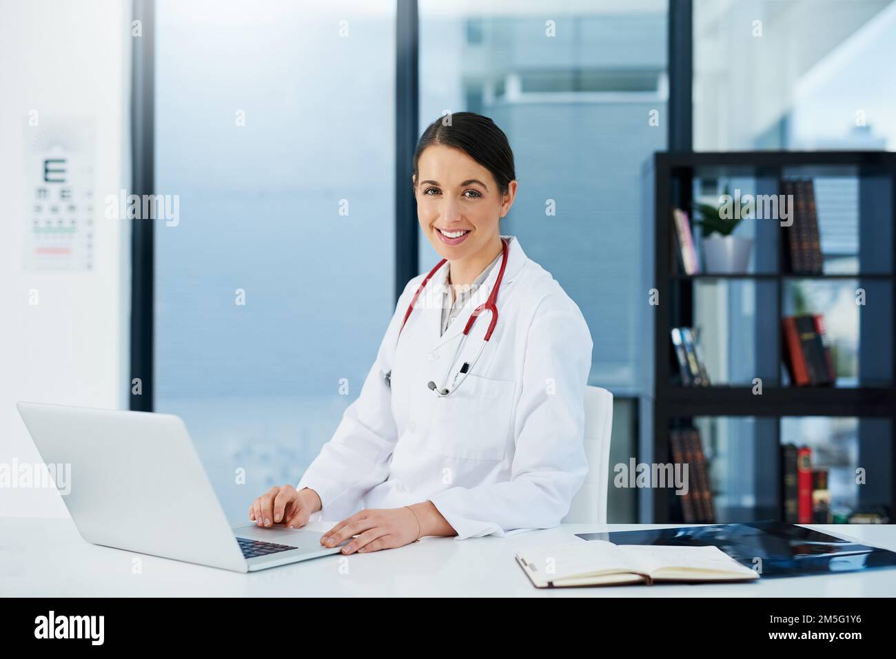 Das lächelnde Gesicht des Arztberufs. Porträt einer jungen Ärztin, die mit einem Laptop am Schreibtisch sitzt. Stockfoto