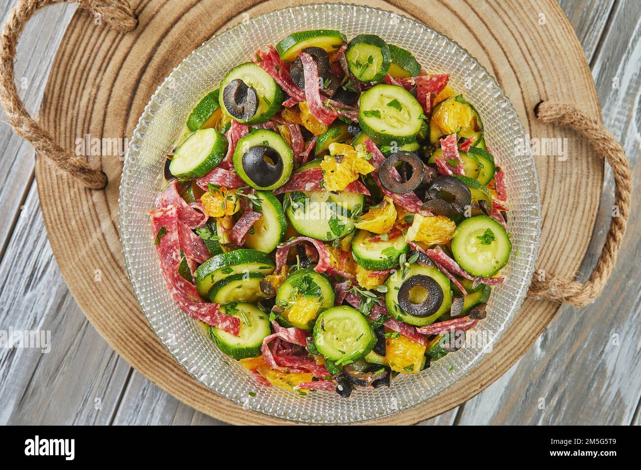 Salat mit Zucchini, Orangen und Salami der französischen Gourmetküche auf Holzhintergrund. Flach verlegt. Stockfoto