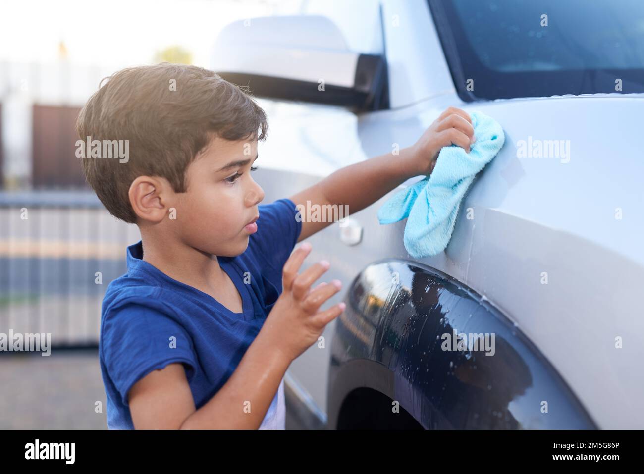 Ich gebe dem Familienauto etwas aufmerksamkeit. Ein kleiner Junge, der zu Hause ein Auto wäscht. Stockfoto