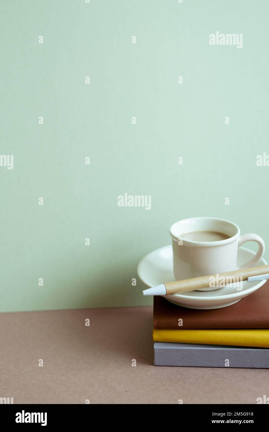 Stapel Notizbuch und Stift, Tasse Kaffee auf dem Schreibtisch. Mintfarbener Wandhintergrund. Workspace, Kopierbereich Stockfoto