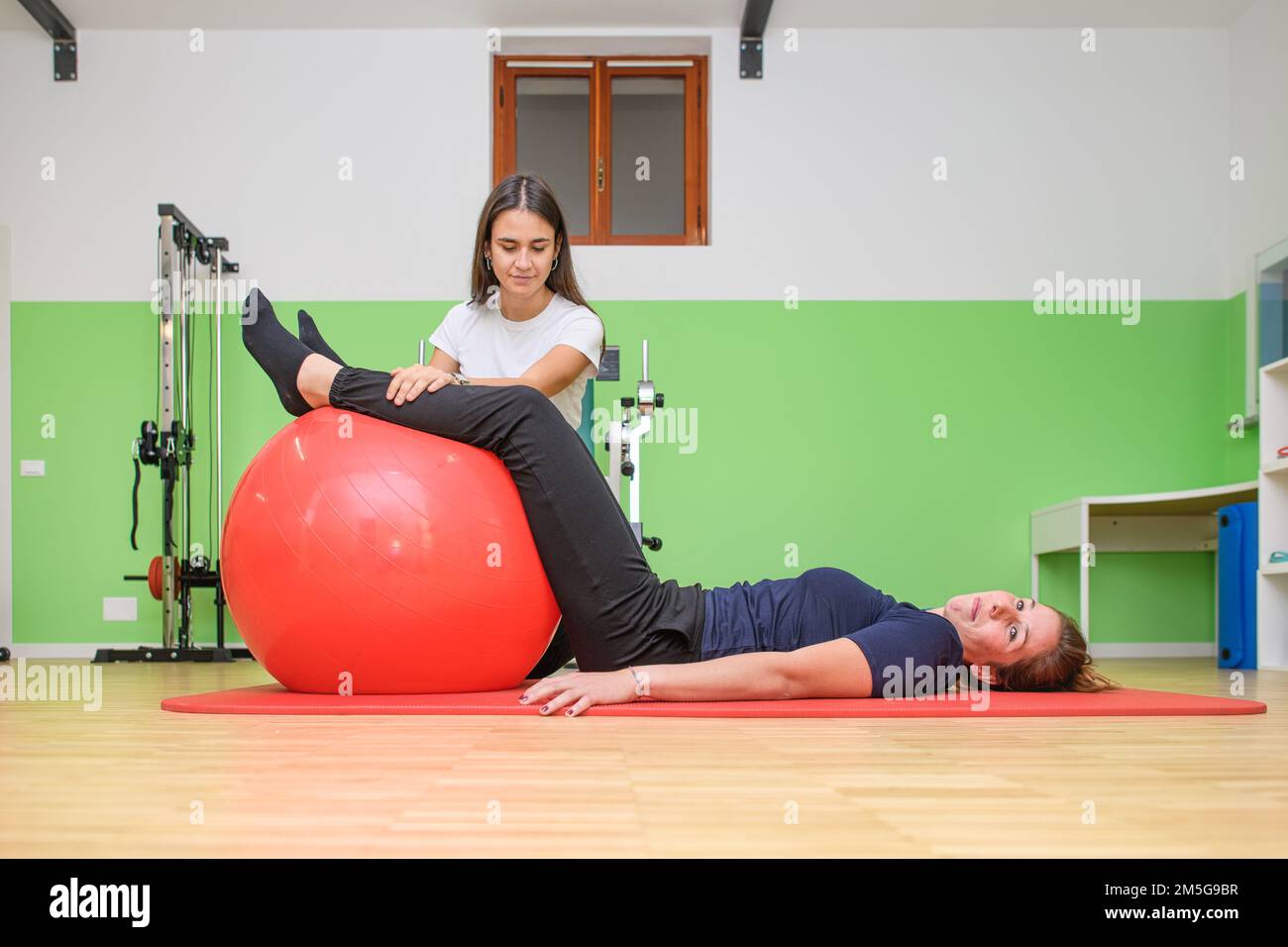 Ein Physiotherapeut lässt seinen Patienten eine Übung der Muskelspannung mit dem Fitnessball durchführen Stockfoto