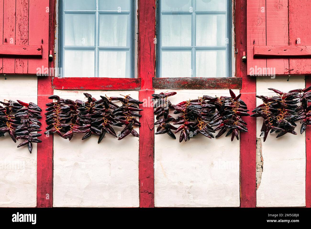 Chili-Paprika, zum Trocknen an der Fassade hängende Espelette, typisches Fenster mit roten Fensterläden, Details, Espelette, Departement Pyrenees-Atlantiques. Stockfoto