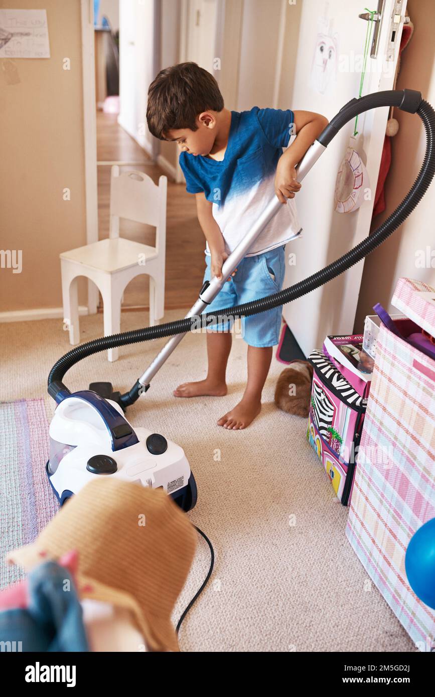 Ich muss sicherstellen, dass ich überall staubsauge. Ein fokussierter kleiner Junge, der sein Zimmer zu Hause mit einem Staubsauger reinigt. Stockfoto