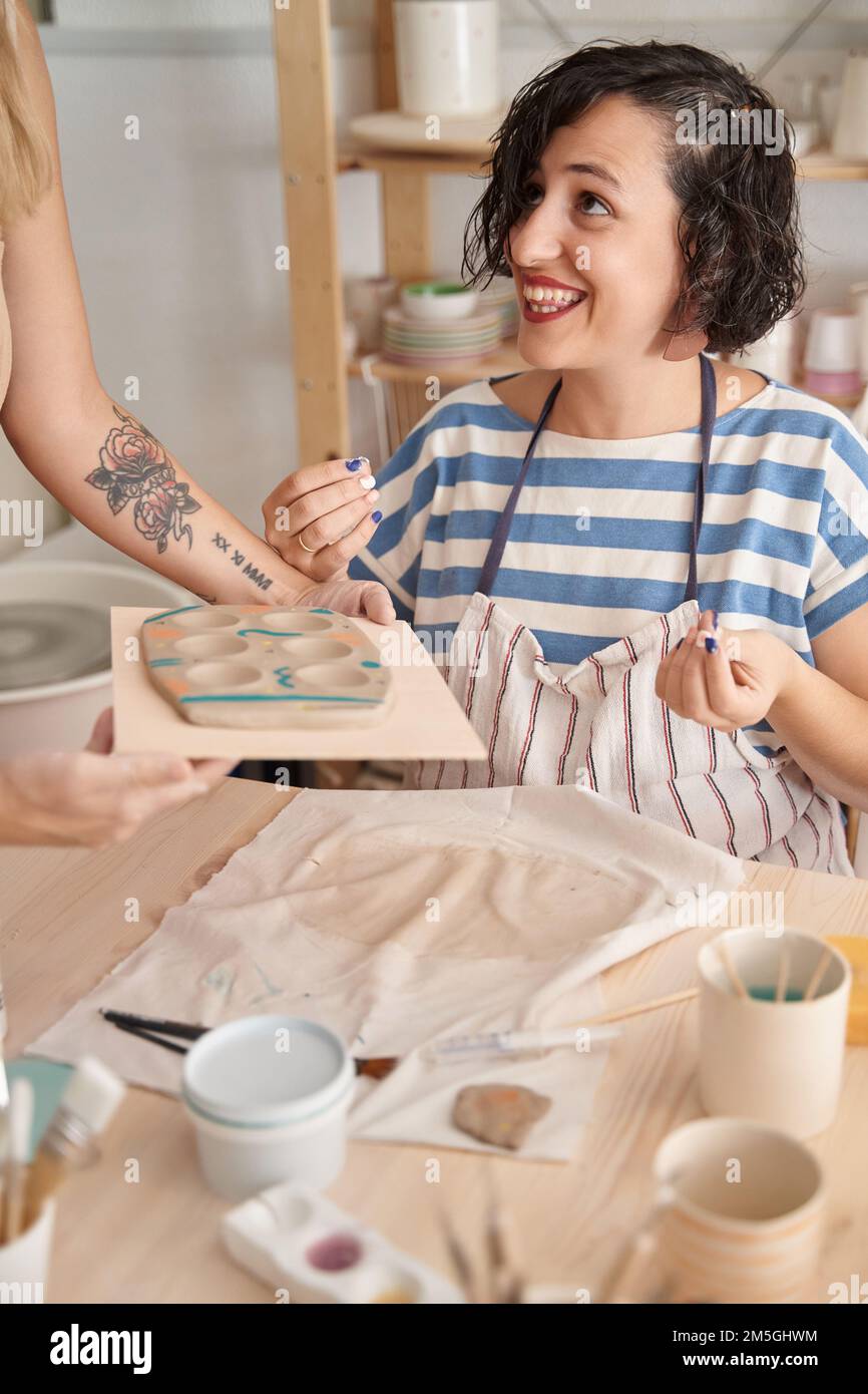 Eine Frau mit Schürze genießt es, während sie Töpferkurs macht. Handwerk, Kunst und Hobbys. Stockfoto