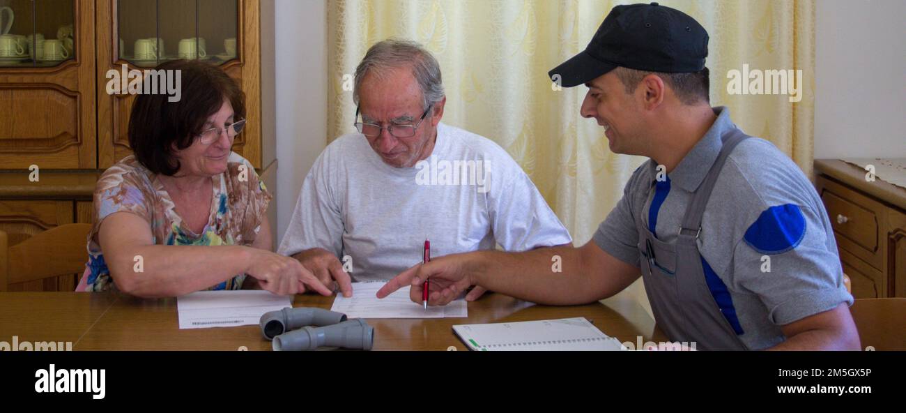 Bild eines Klempnertechnikers, der einem älteren Paar eine Rechnung für die zu erledigende Arbeit vorlegt. Unterzeichnung und Festlegung des Arbeitsvertrags. Stockfoto