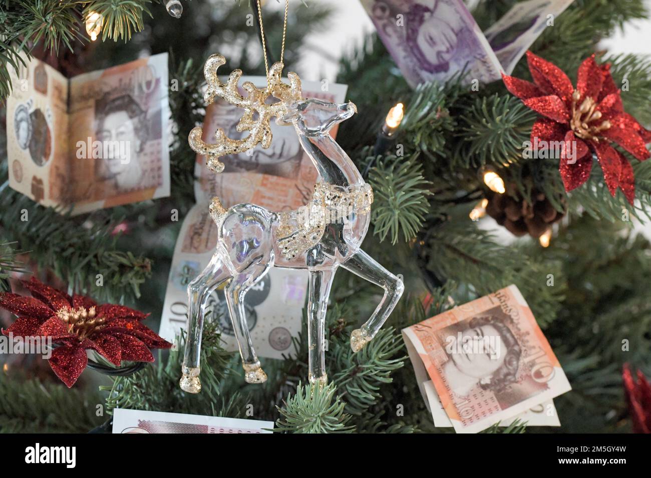 Weihnachtsbaum mit 10 Pfund und 20 Pfund Noten als Dekoration mit einem Glas und goldenen Rentier im Vordergrund, teure Weihnachten Stockfoto