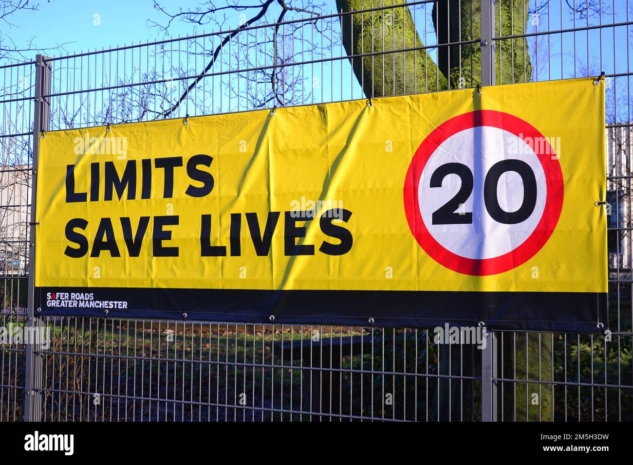 Auf dem Banner für Geschwindigkeitsbegrenzungen steht „Limits Save Lives“ mit einem Vorschlag für 20 km/h am Zaun einer Schule in Manchester, Großbritannien Stockfoto