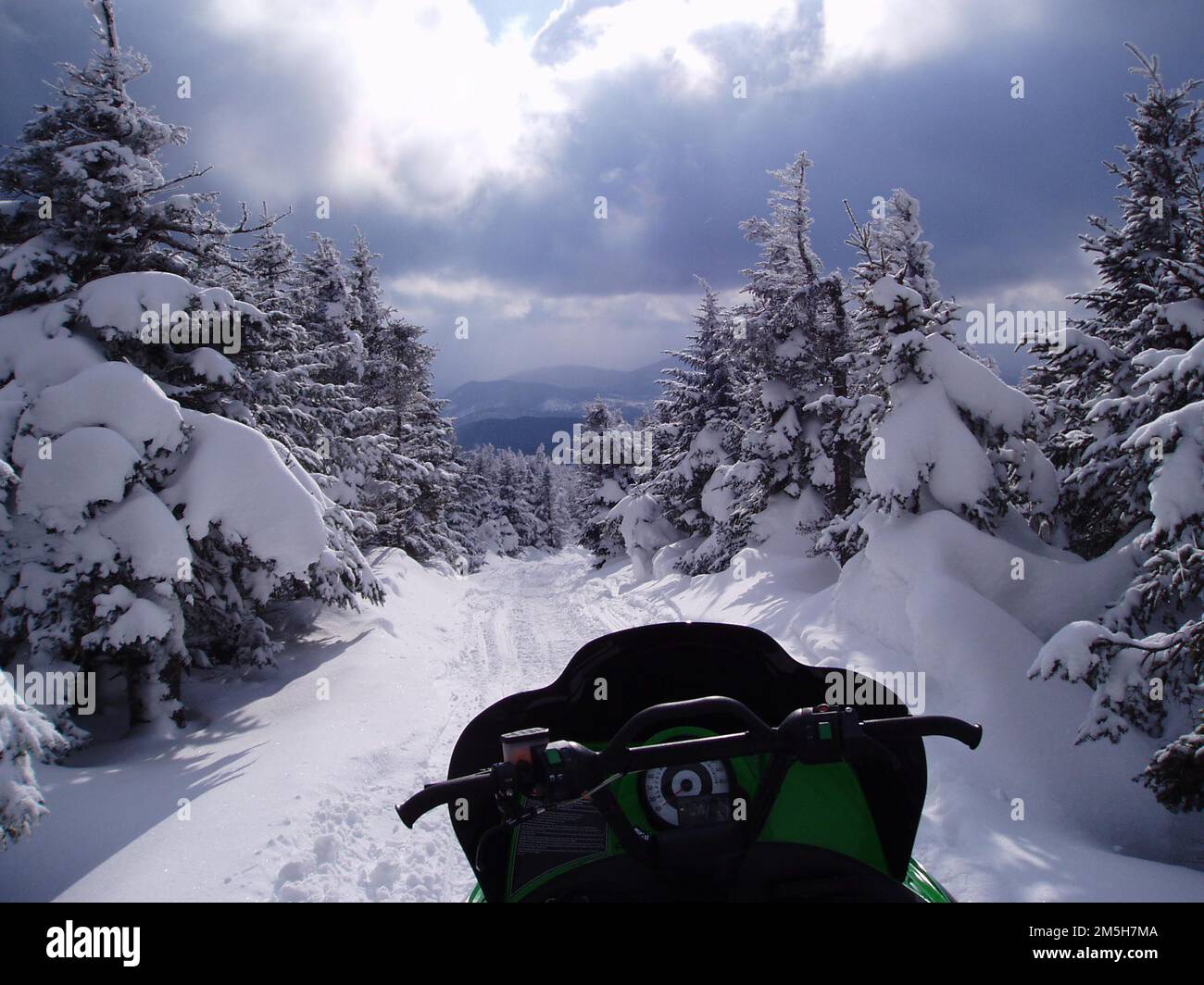 Rangeley Lakes Scenic Byway - The Trail lockt - lassen Sie das Abenteuer beginnen! Ein wunderschöner, wolkiger Himmel lädt diesen Schneemobilfahrer ein, einen großartigen, verschneiten Tag in Maine zu genießen. Lage: Maine Stockfoto