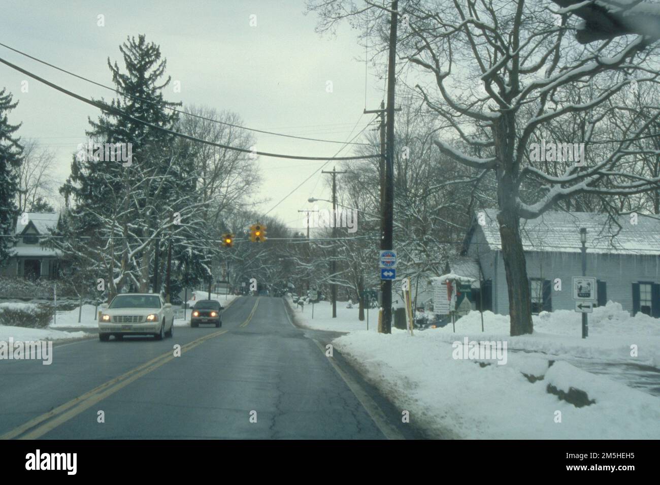 Ohio & Erie Canalway - Fahrt durch ein winterliches Viertel. Im Winter fahren zwei Autos durch eine Kreuzung in einem Wohngebiet. Ein kleines weißes Haus auf der rechten Seite blockiert die Kälte. Standort: Ohio & Erie Canalway, Ohio (41,241° N 81,551° W) Stockfoto