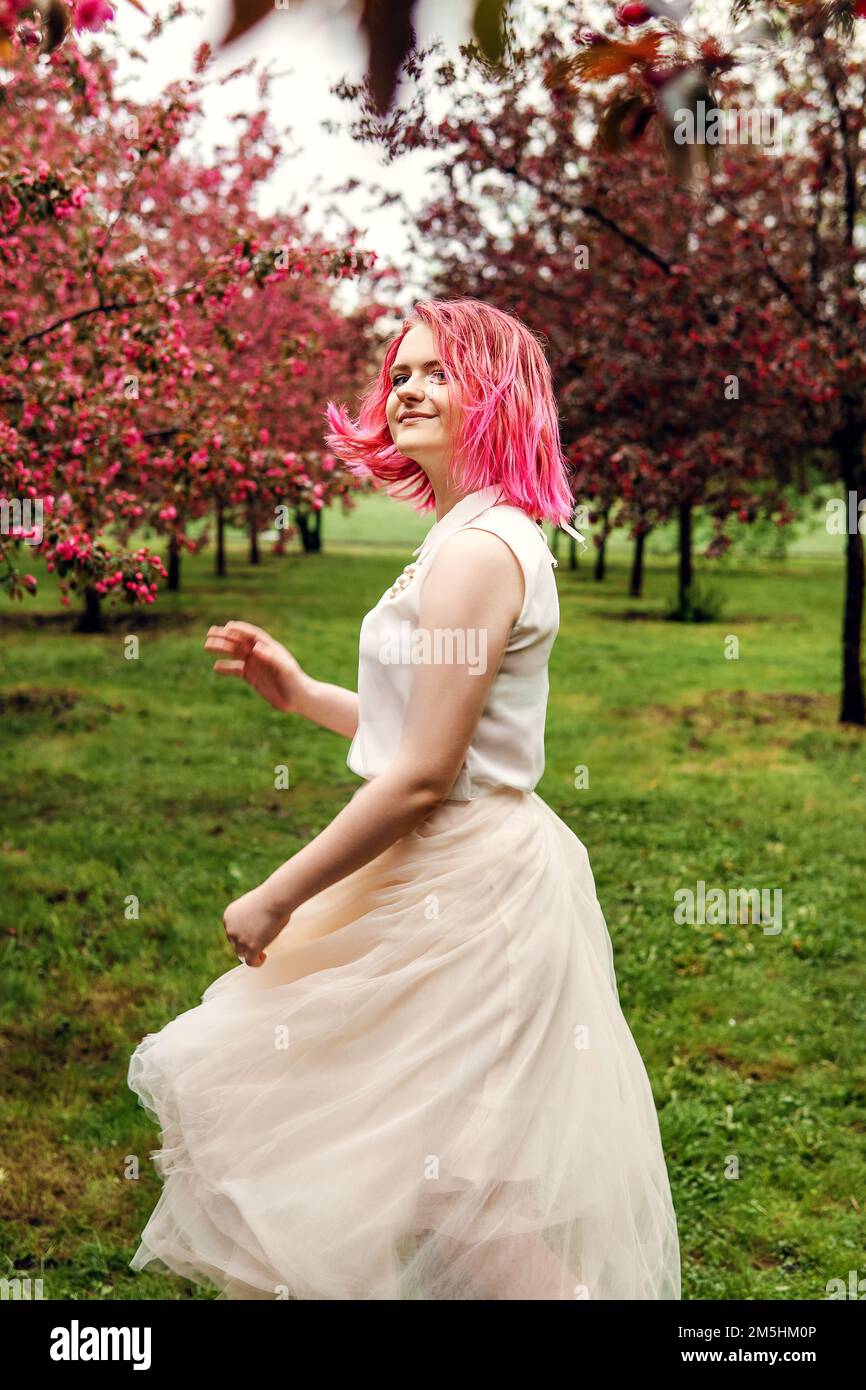 Ein junges Mädchen mit rosa Haaren in einem Apfelgarten. Hübsches junges Mädchen in einem blühenden Garten aus rosa Apfelbäumen Stockfoto