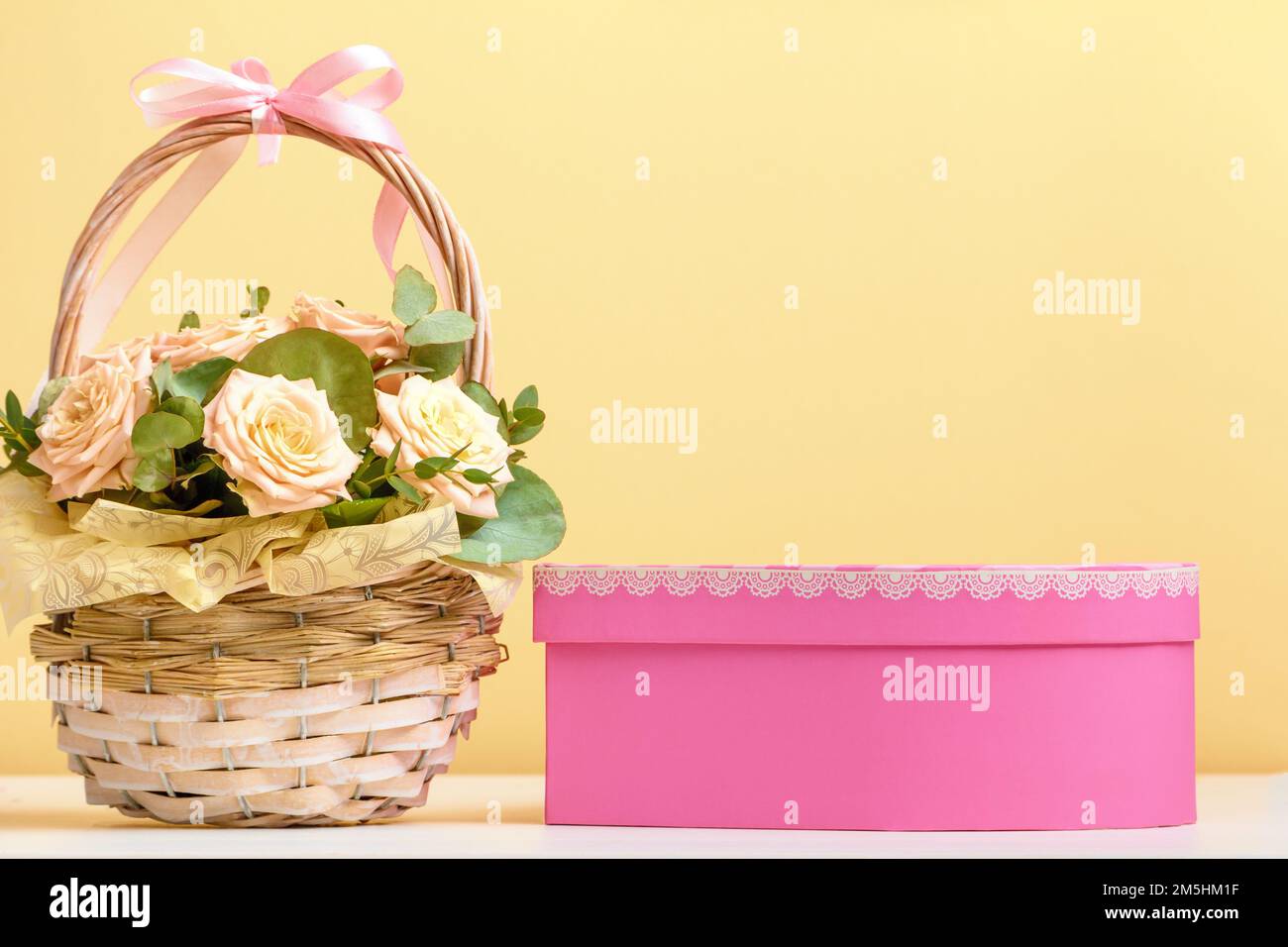 Valentinstag, Muttertag, Geburtstag. Blumen in einem Korb und eine rosa Schachtel mit einem Geschenk auf dem Tisch. Stilllebensraum Stockfoto