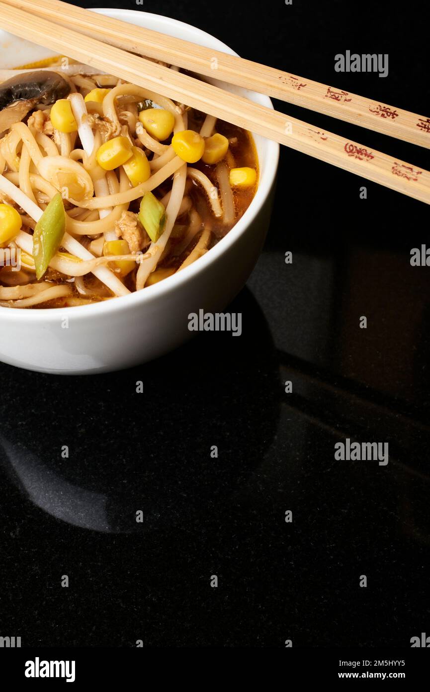 Eine Schüssel mit chinesischem Huhn und Zuckermaissuppe in einer weißen Schüssel mit Stäbchen auf schwarzem Hintergrund. Studioaufnahme. Stockfoto